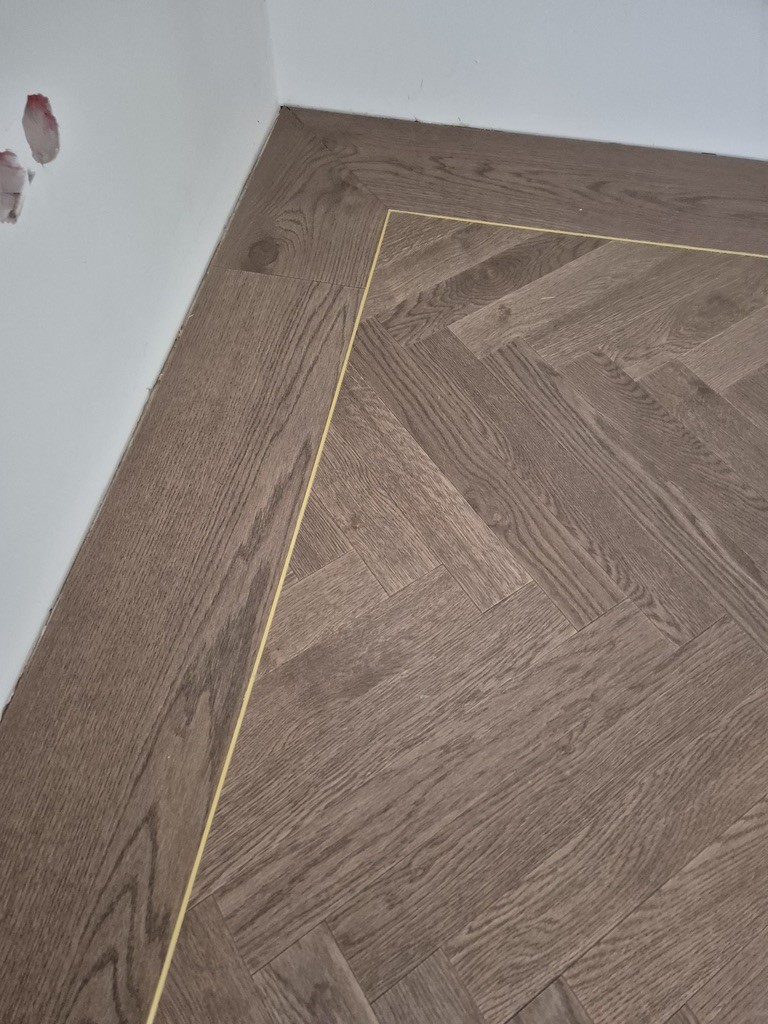 Narożnik mosiężnej intarsji między jodełką a fryzem – detal realizacji Deska Design