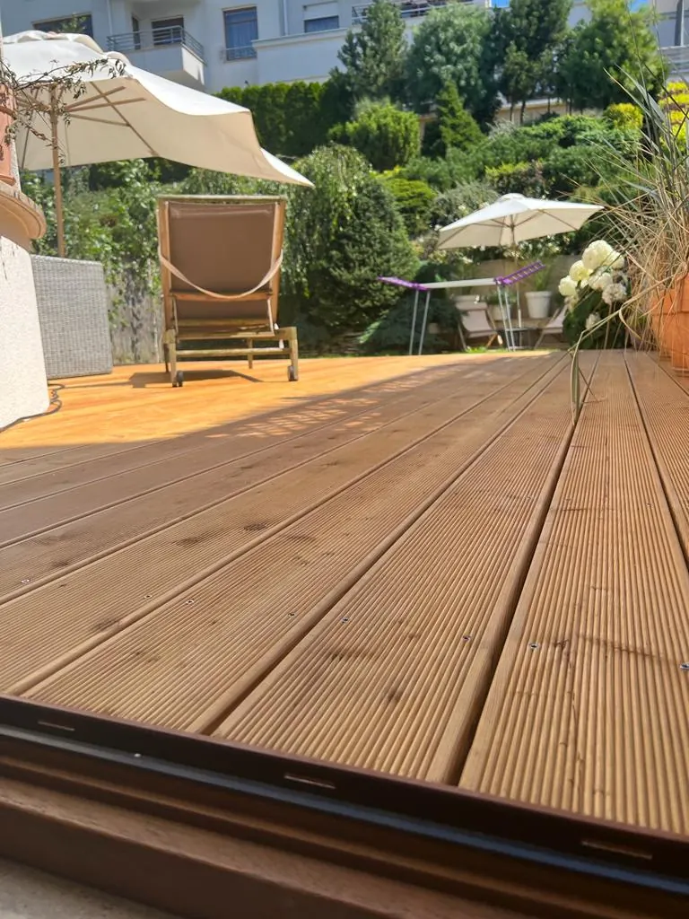 Ryflowany taras drewniany w ogrodzie Ryflowany taras drewniany w ogrodzie z leżakiem i parasolem – realizacja Deska Design